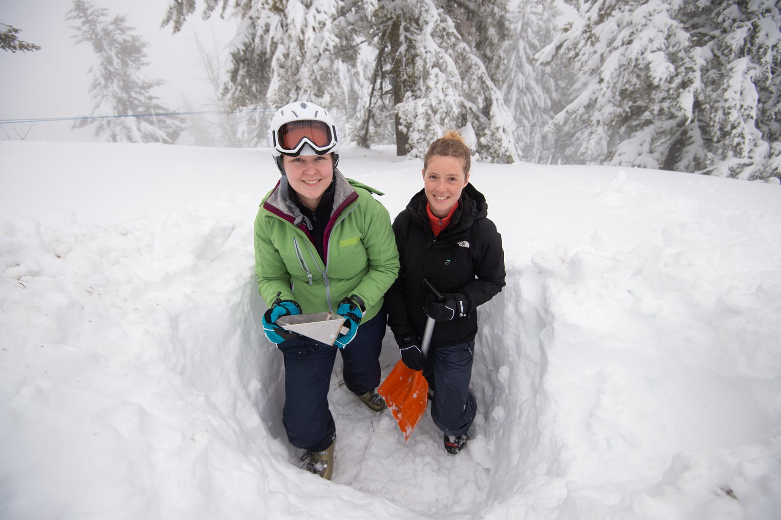 Two students hold shovel and clipboard in snow pit
