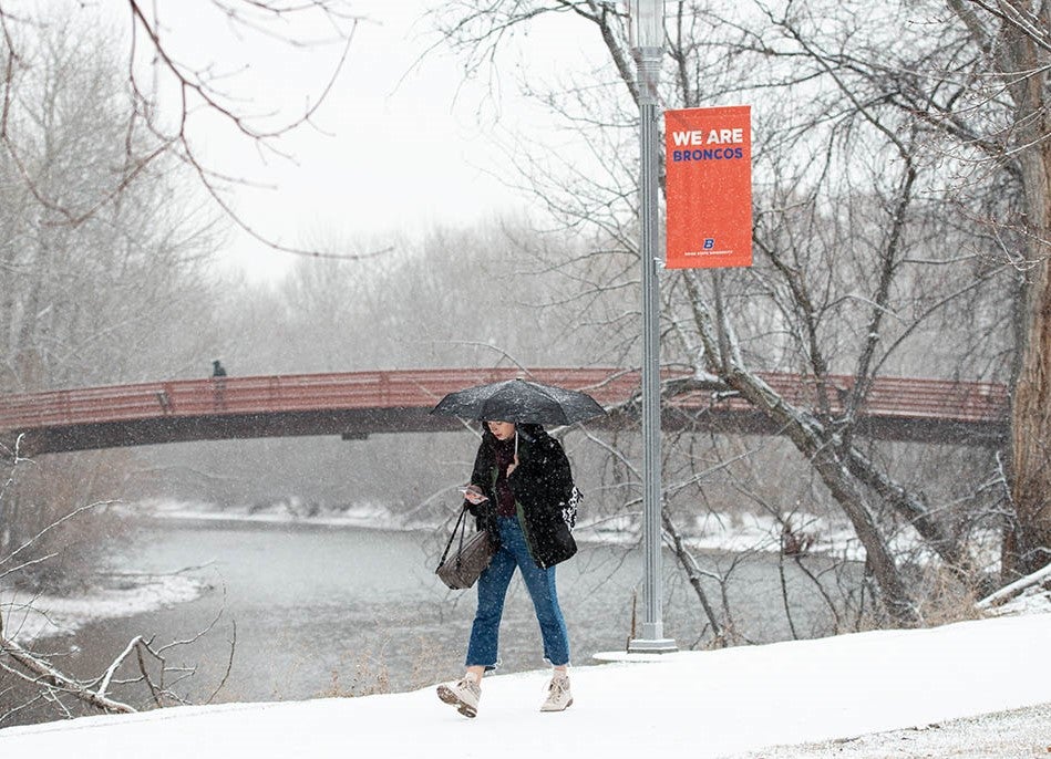 Student walks through the snow, We Are Broncos banner behind her