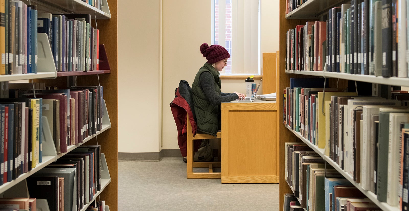 Student framed by bookshelves sits at the library 