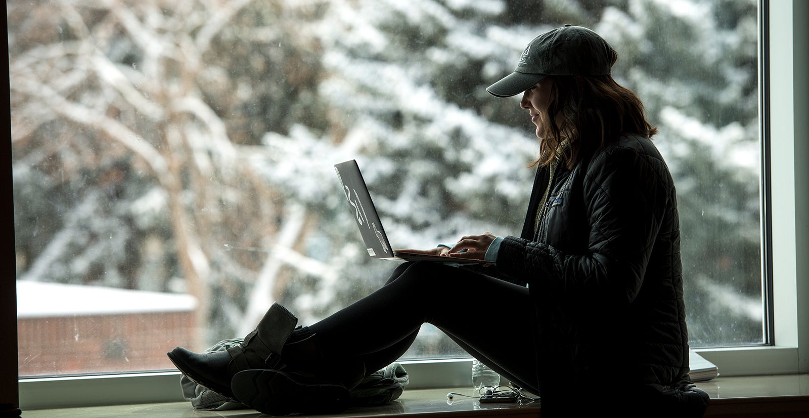 student working on laptop while sitting by a window with a snowy scene