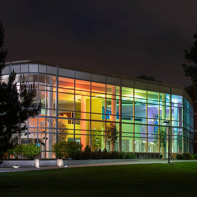 Glass-faced atrium of the Student Union Building, illuminated from within in colorful lights against a dark night sky.
