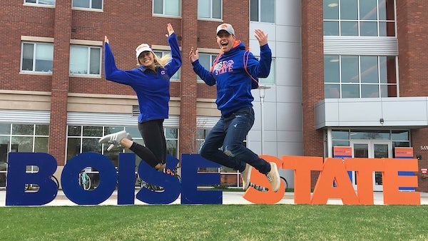Two students jumping in sync in front of a Bosie State sign