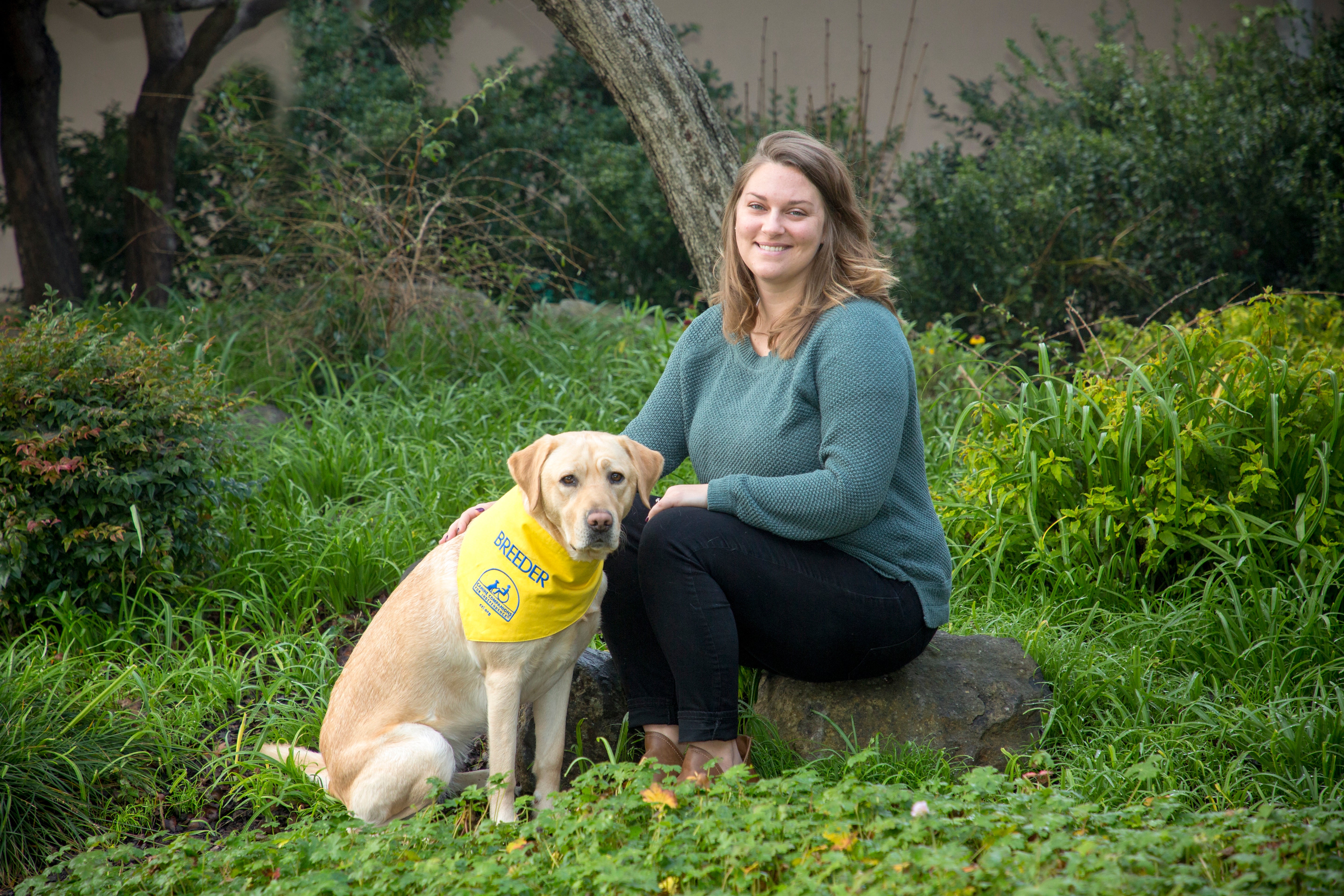 Kim sits next to a yellow lab who is wearing a yellow breeder bandana