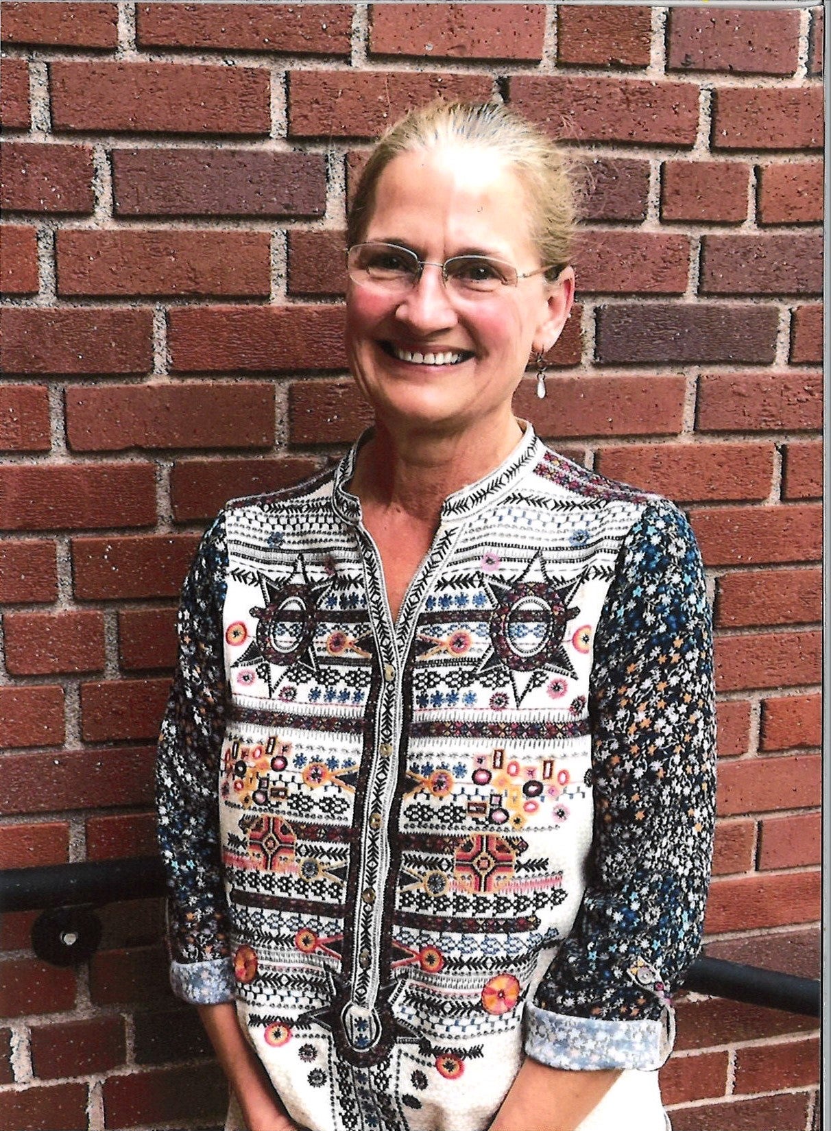 Katherine Kappelman smiling against a brick wall wearing a black and white patterned top