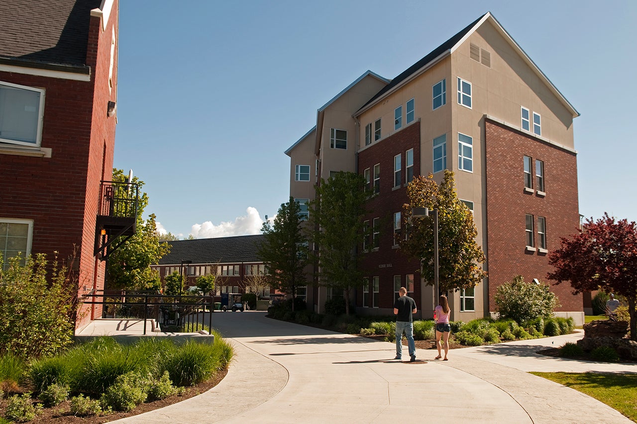 Multi-story brick dormitory with two students on sidewalk