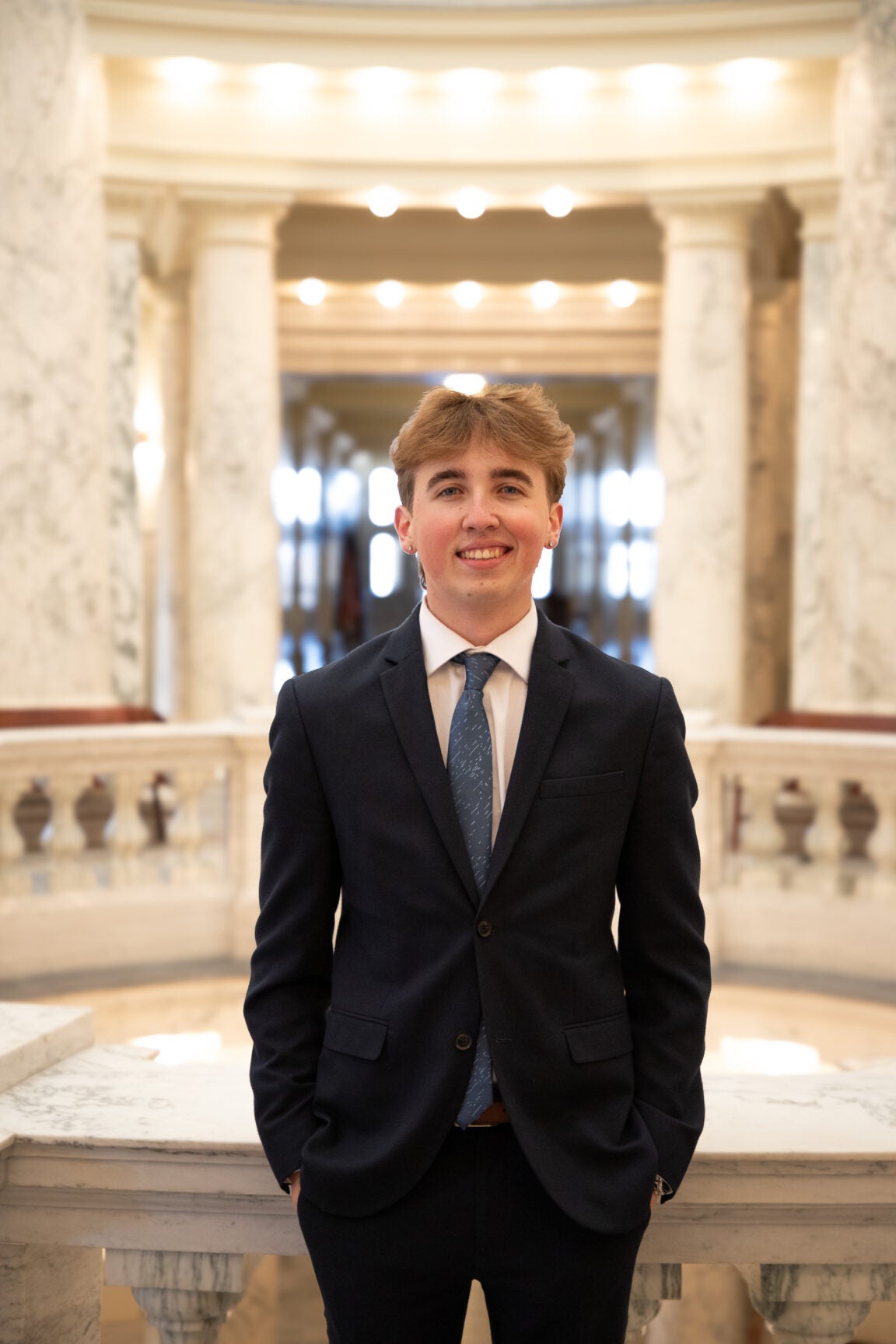 Mason Magee wearing a suit with his hands in his pockets, smiling, standing in the rotunda of the Idaho state capitol.