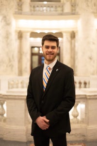 Austin standing in Capitol rotunda smiling in a suit