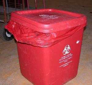 example of improper biohazard bin use: shows a red biohazard bin with a waste bag protruding under the lid