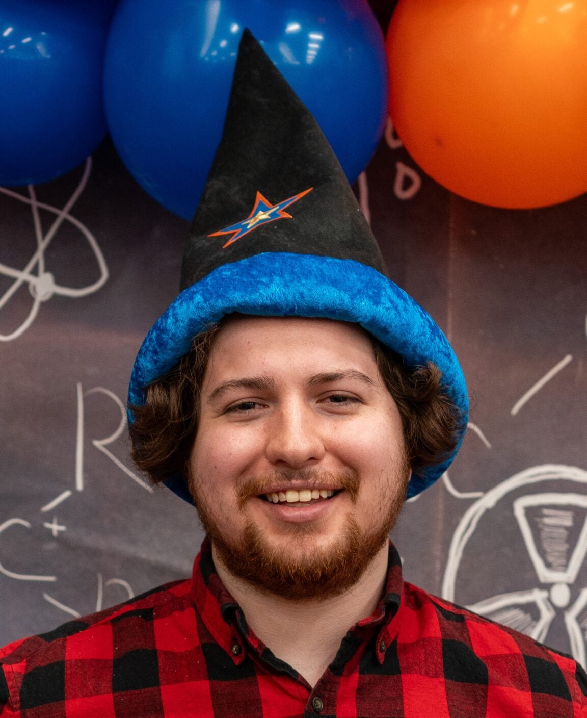 Photo of Antonio Reyes in a wizard hat with blue and orange balloons behind him