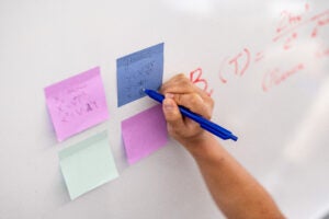 Students writing on sticky notes stuck to a whiteboard.