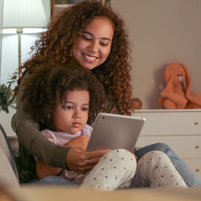 A woman and child engage with an iPad in a bedroom