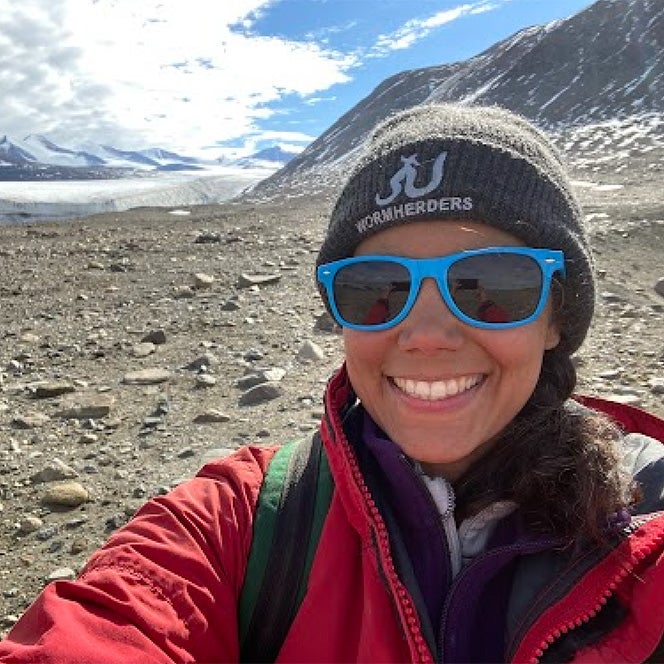 Photo of Melisa Diaz from the University of Colorado Boulder standing in a mountain pass with a glacier behind her