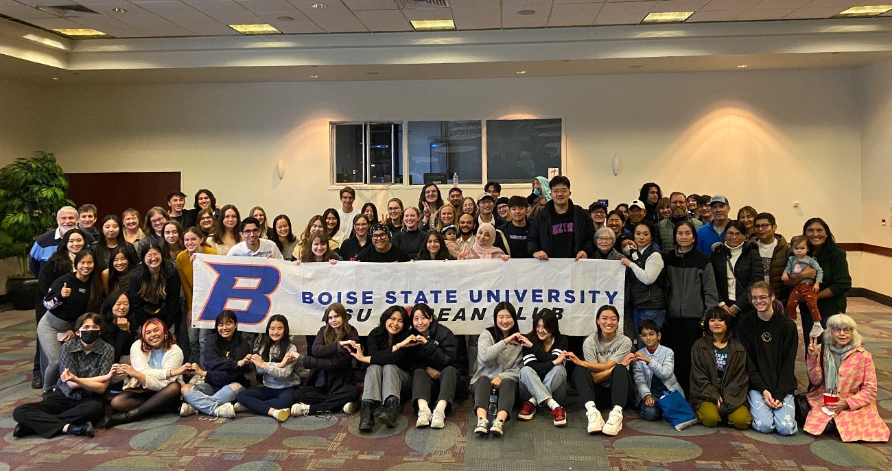 Participants of the annual Korean Club BBQ at Boise State standing and sitting for a photo in a room in the Student Union holding a banner with the words "Boise State University Korean Club"