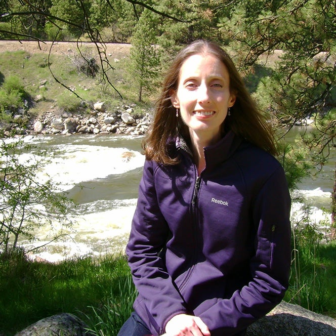 Cheryl Hindrichs sitting on a rock beside a river
