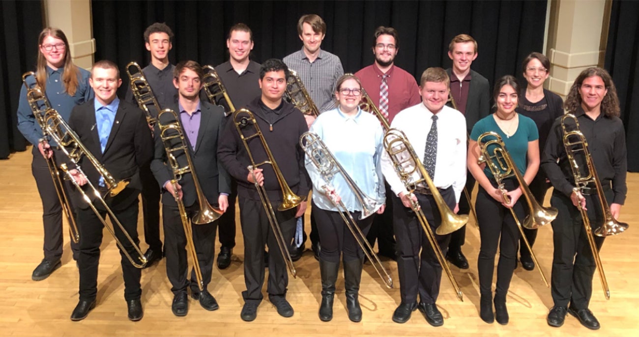 Photo of 14 members of the Boise State Trombone Choir on a stage with trombones in their hands