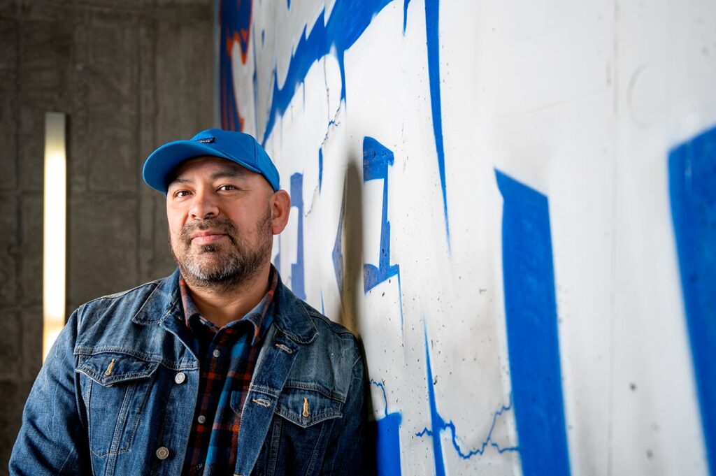 Portrait of Bobby Gaytan in front of his artwork
