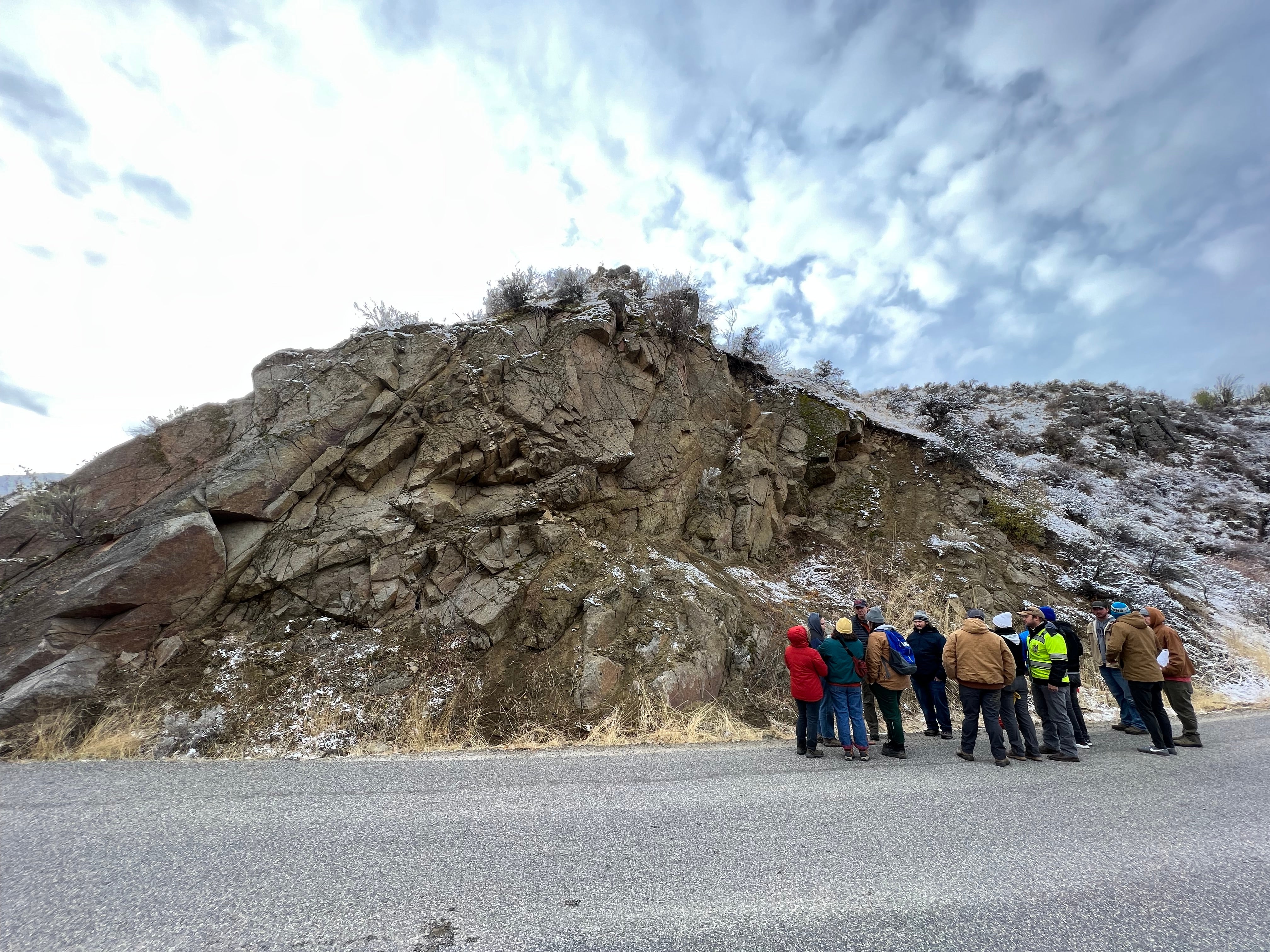 group of people standing on road in front of large rocky slope