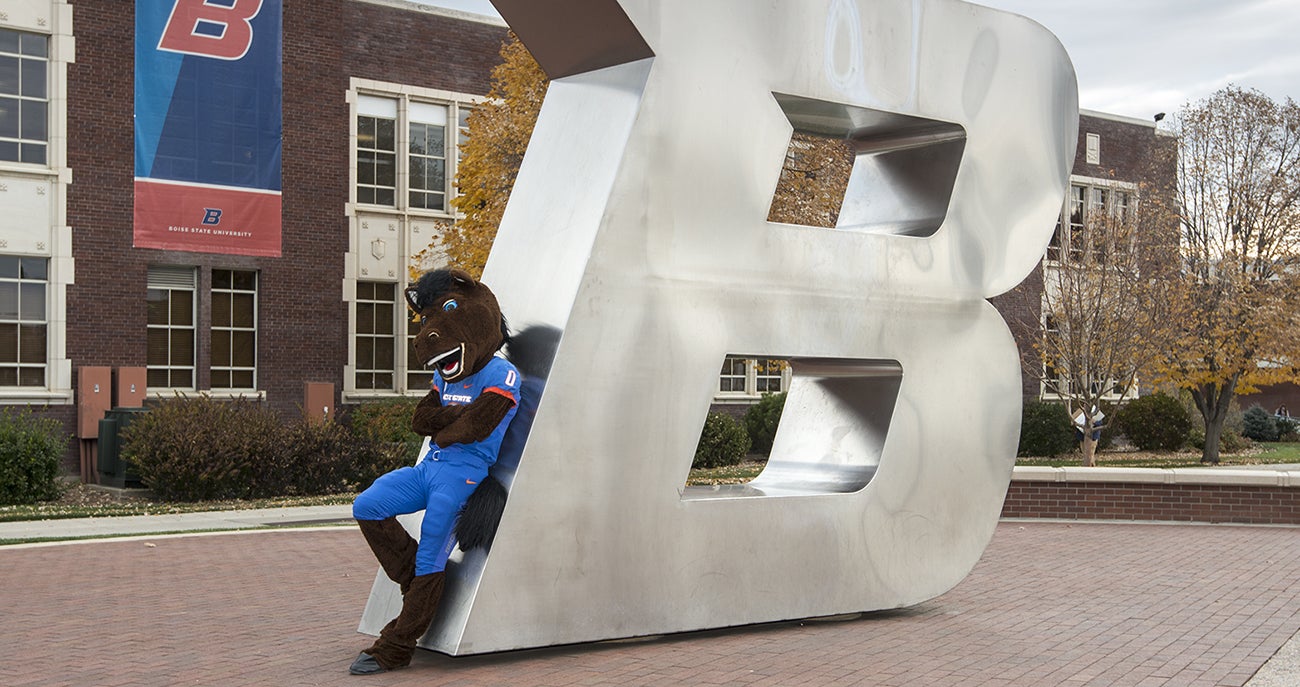 Buster Bronco leaning against the B on campus