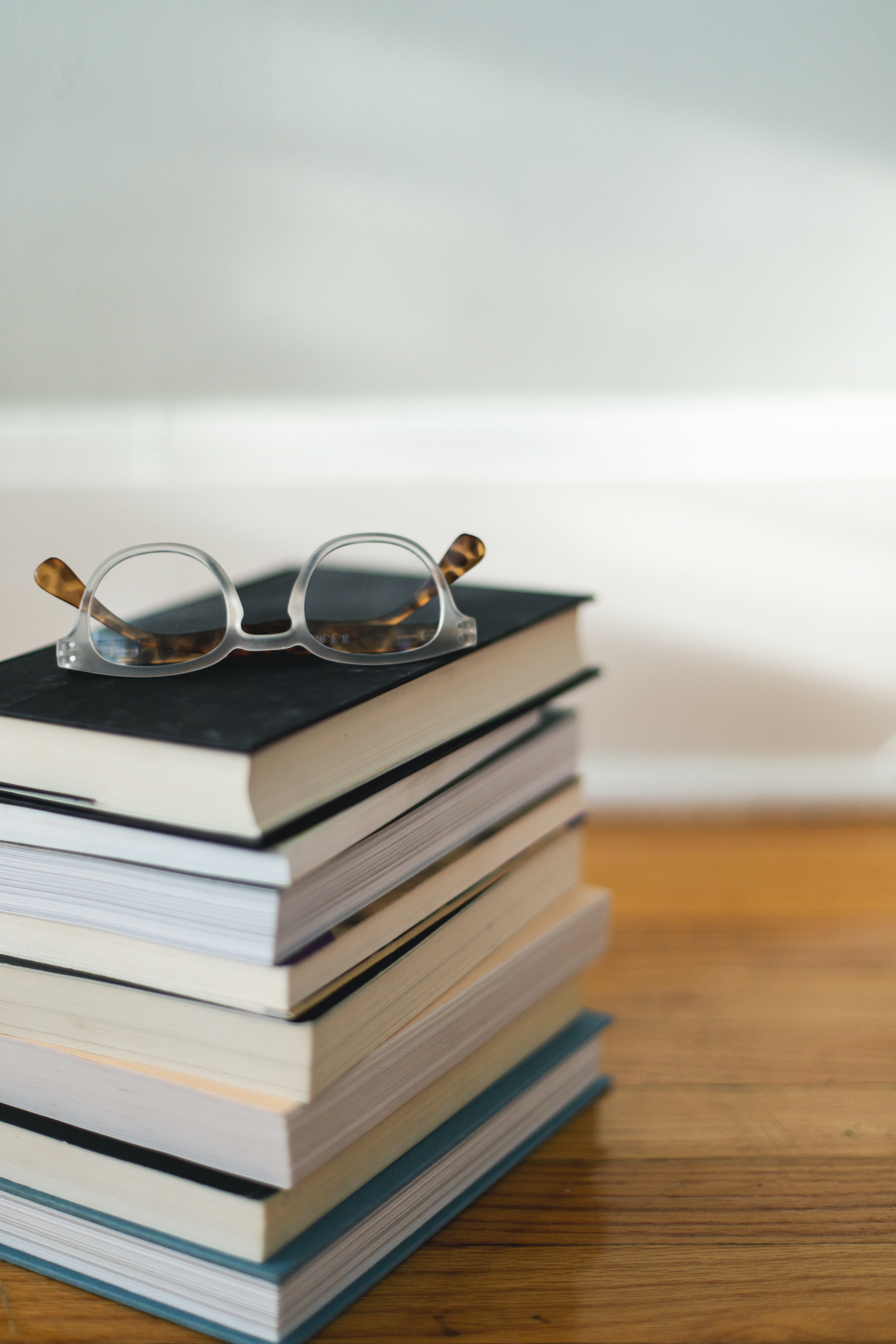 Stack of books resting on table, with reading glasses on top.