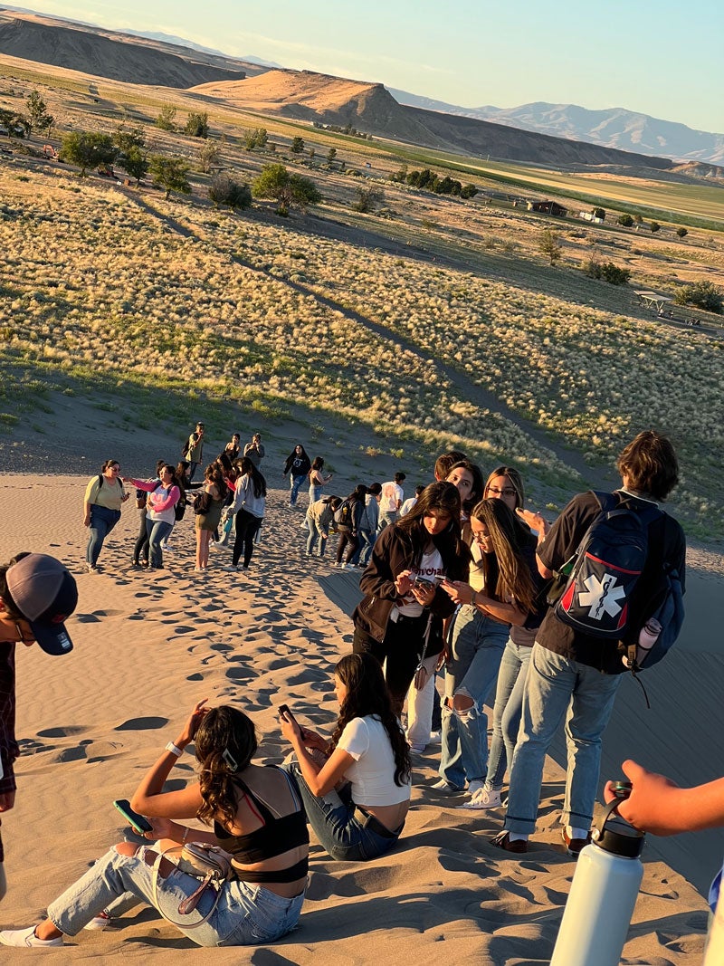 Photo of Upward Bound students sitting and standing on a sand dune in evening light