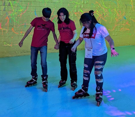 Photo of three TRIO Upward Bound students holding hands while roller skating