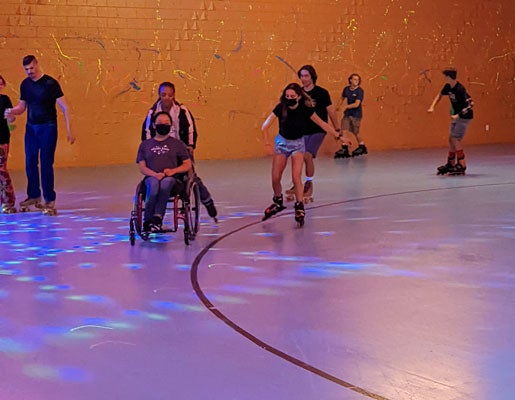 Photo of two female TRIO Upward Bound students, one in a wheel chair and the other pushing on roller skates. 