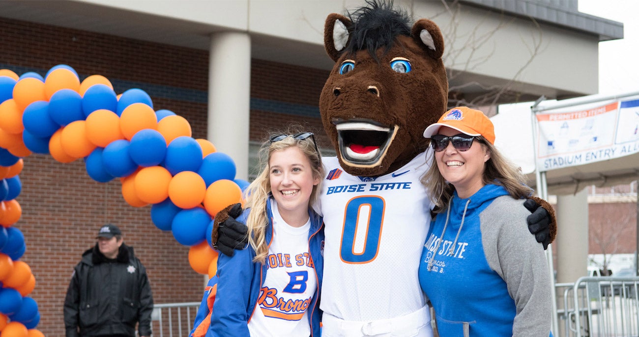 Buster Bronco stands with a Boise State student and a parent
