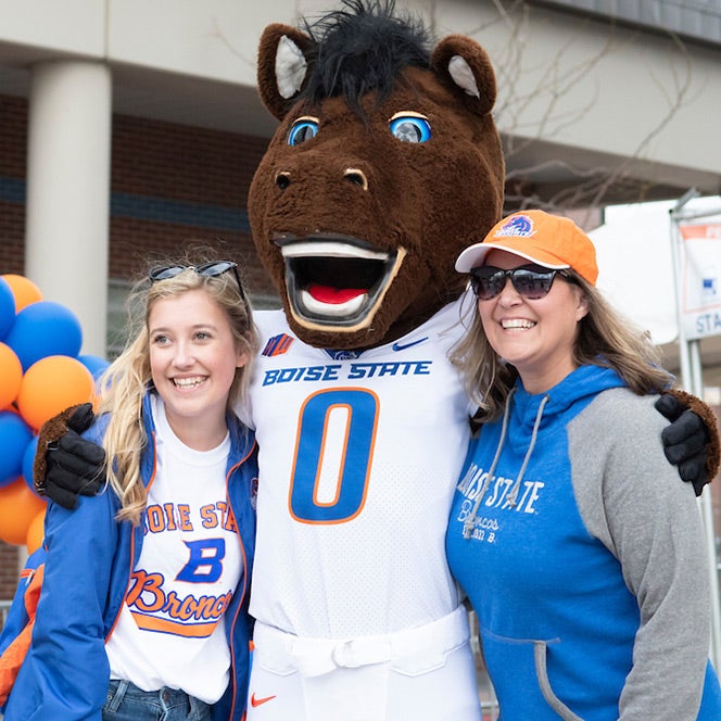 Buster Bronco stands with a Boise State student and a parent