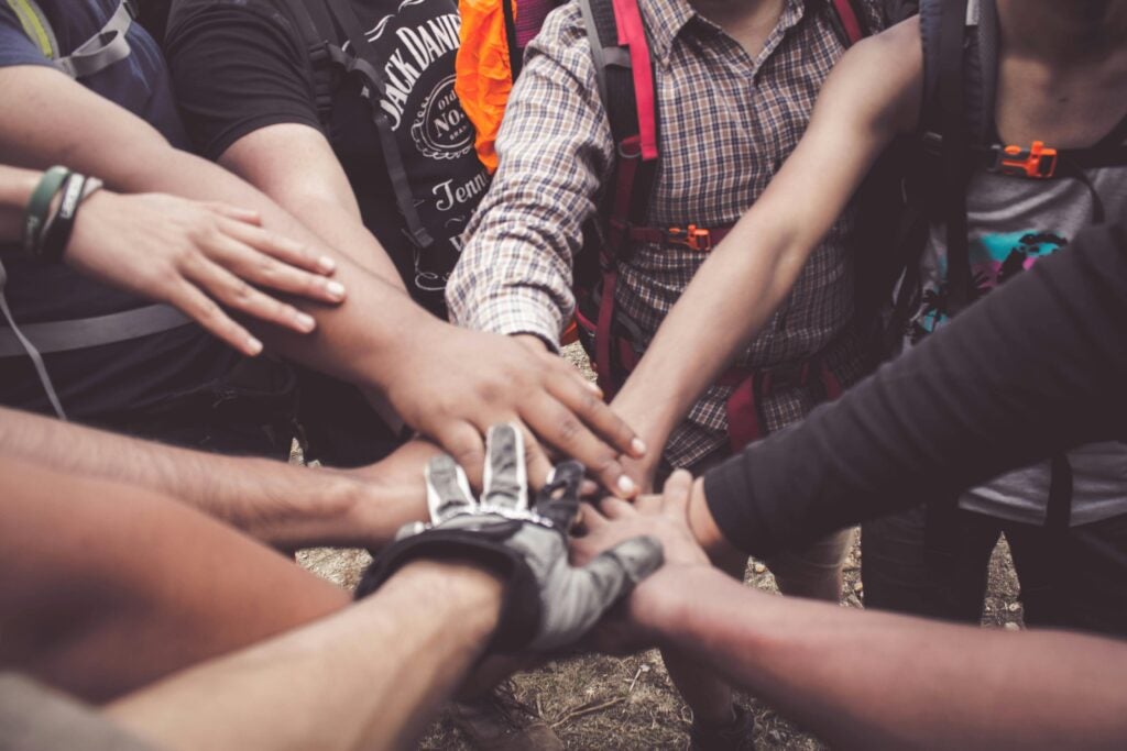 A group of people with hands piled together, some wearing backpacks.