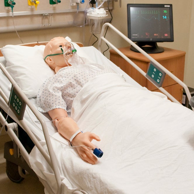 A Hal high fidelity manikin wearing an oxygen mask sits in a hospital bed