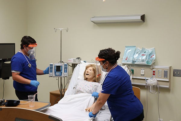 Nursing students wearing facial masks and face shields treat a manikin in the Simulation Center