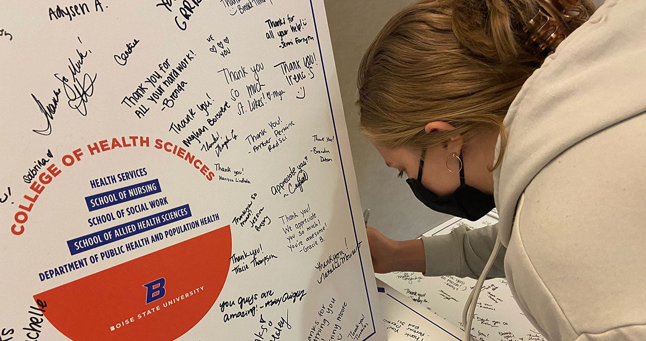 student signs giant thank you cards to local health systems