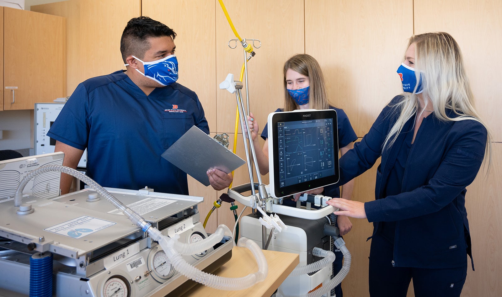 One male, two female respiratory care students gather around a mechanical ventilator