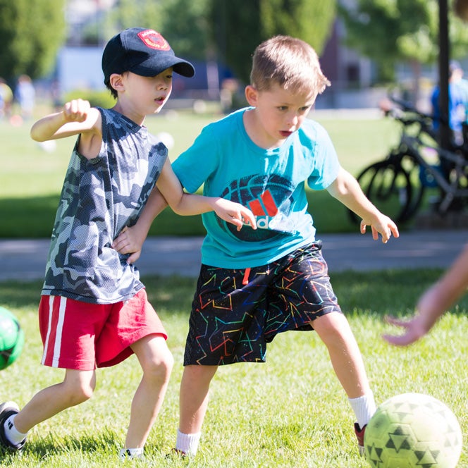 Two young boys play soccer on campus during Summer Youth Sports program