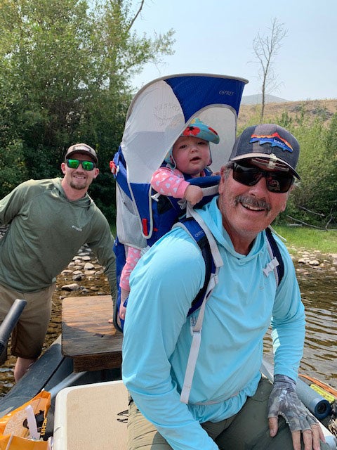 Ken Bell at a dock in a boat with a male friend and grandbaby strapped to his back