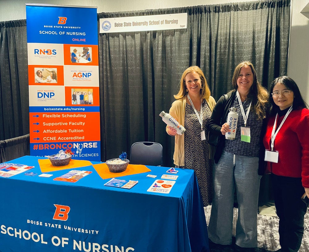 Professors Kelley Connor, Cara Gallegos, and Luzy Zhao stand by a School of Nursing table display.