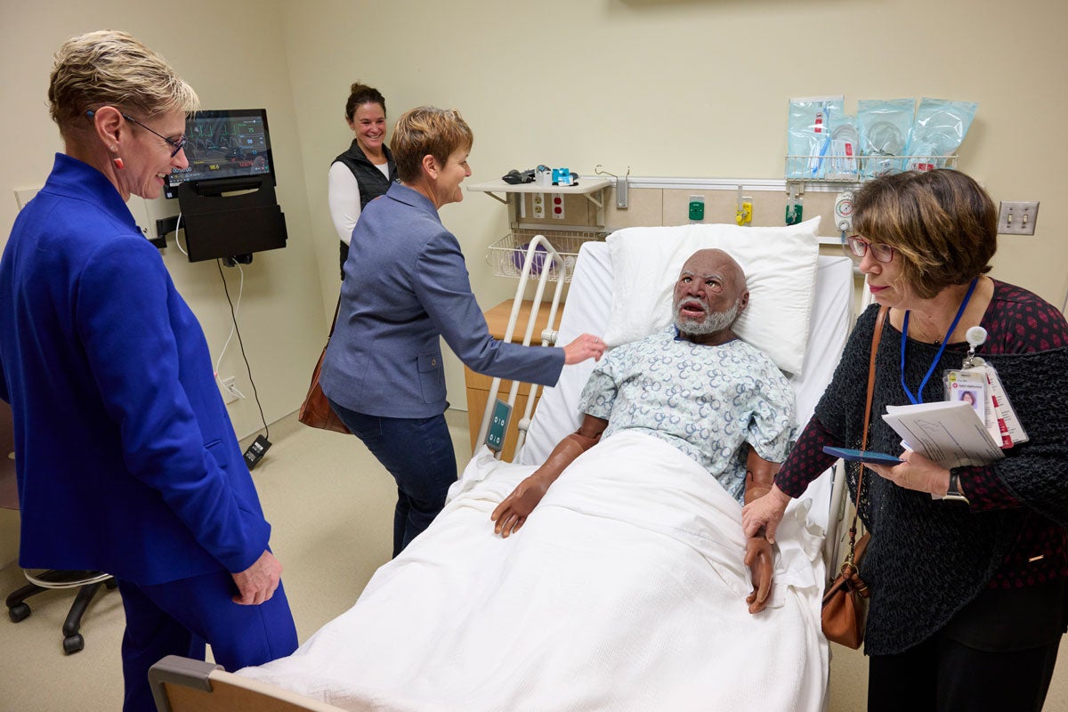 Women stand around a manikin on a hospital bed and feel its pulse.
