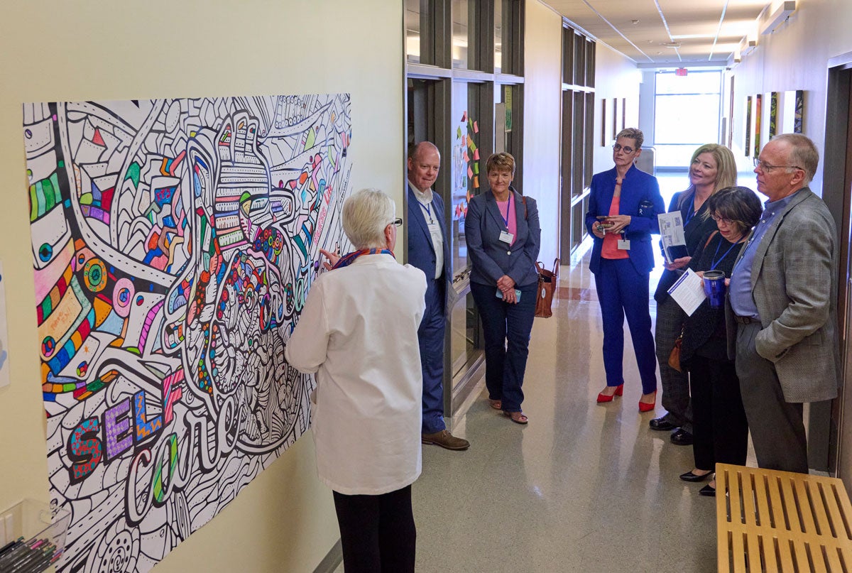 Guests stand in the hallway by a coloring wall mural at the School of Nursing.