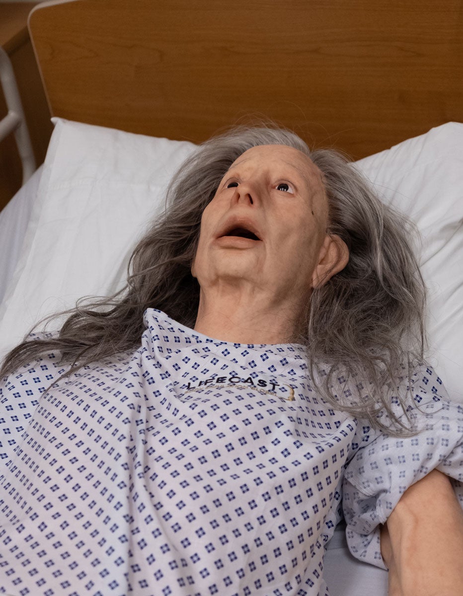 An elderly manikin lies with her mouth open in an eerie stare.