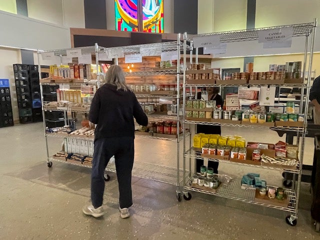 A woman selects groceries from a shelf of food at a food pantry.