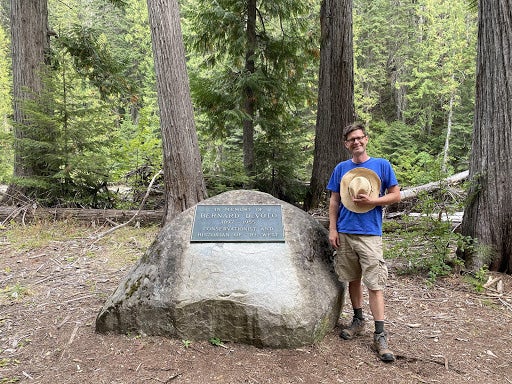 photo of Bob standing next to rock with a plaque that reads In memory of Bernard DeVoto 1897-1955 conservationist and historian of the west
