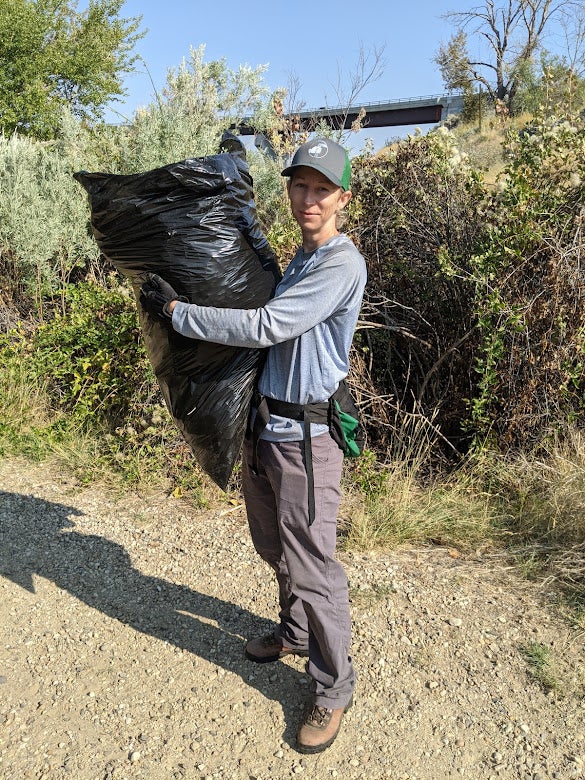 a woman carries a giant trash bag in her arms that is filled to the brim with weeds