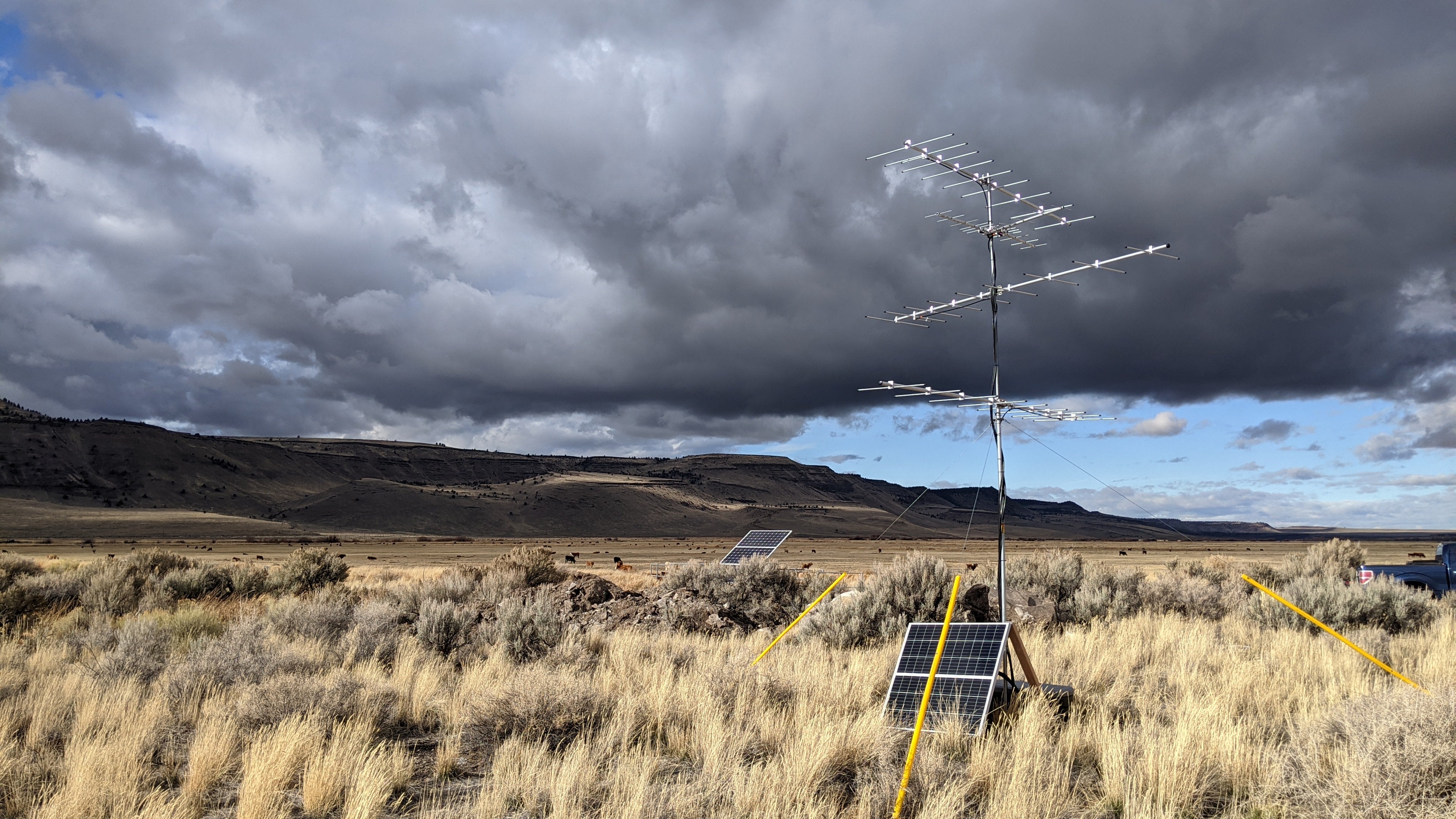 A landscape view of grassy open habitat. A solar panel and antenna are in the foreground, with dramatic gray storm clouds in the background