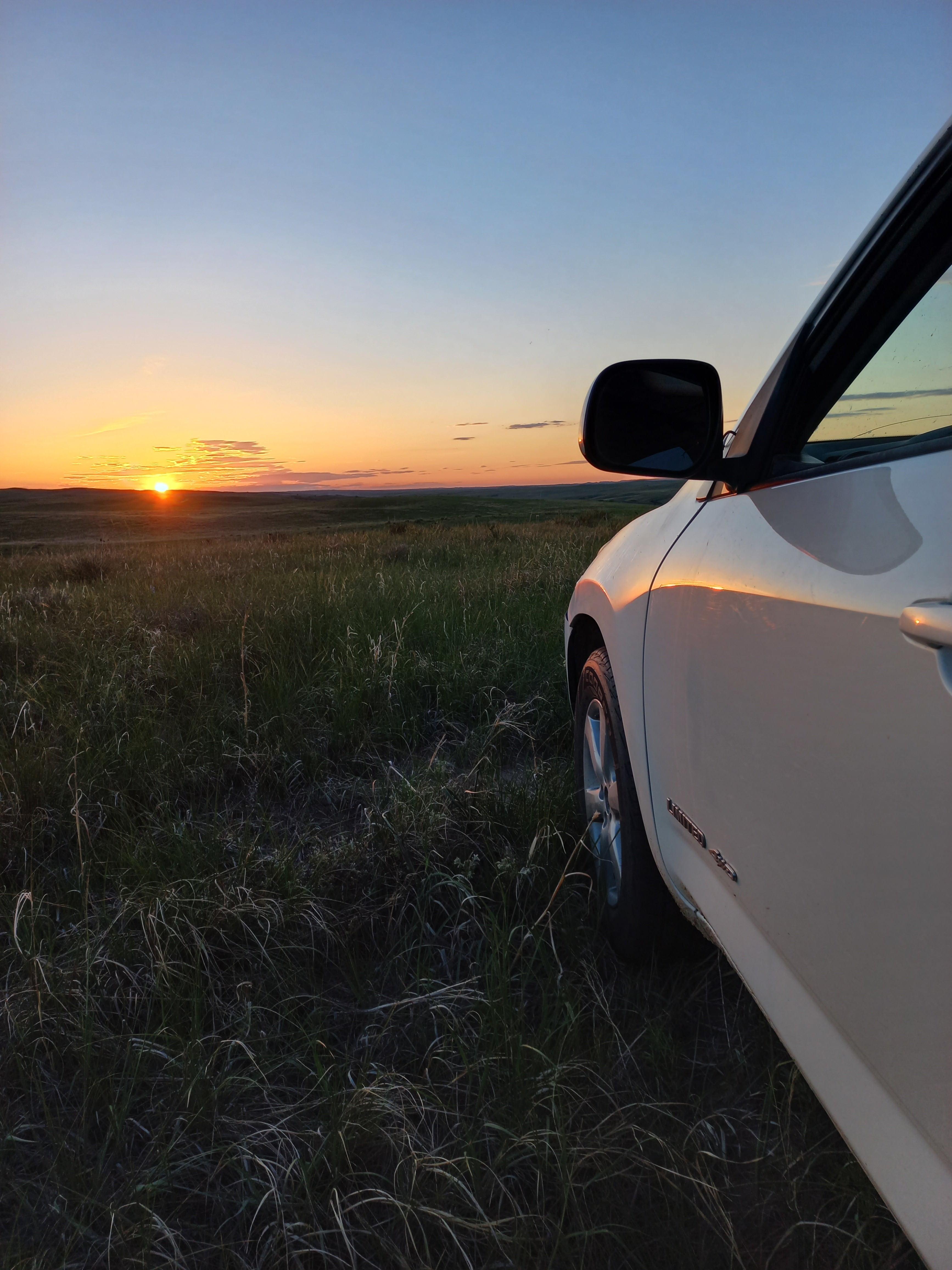 a white vehicle in the grass with the sun cresting the horizon at dawn