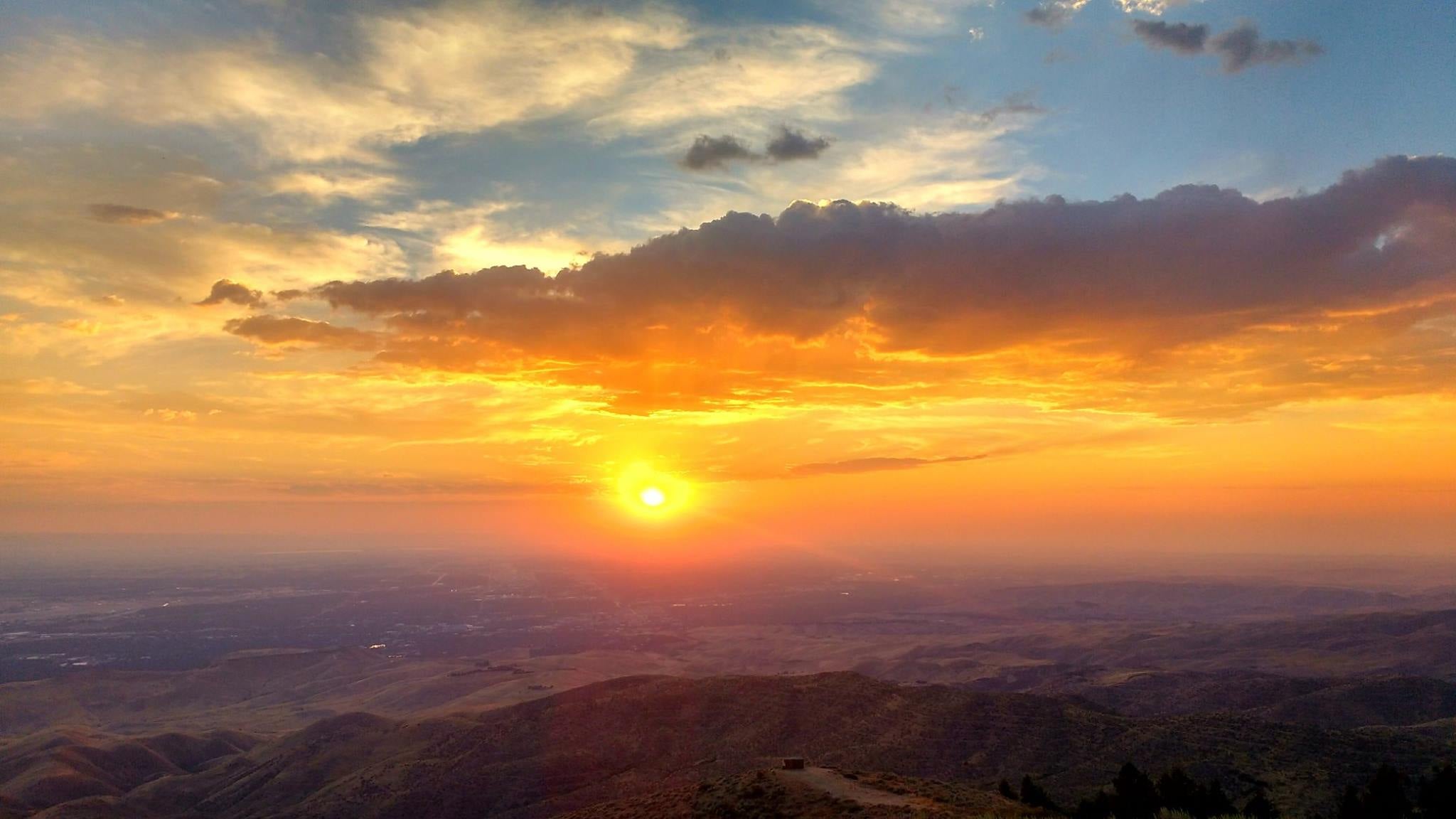 the the view from Lucky Peak looking down over Boise as the sun is setting casting hues of yellow, orange and pink on the clouds over a city