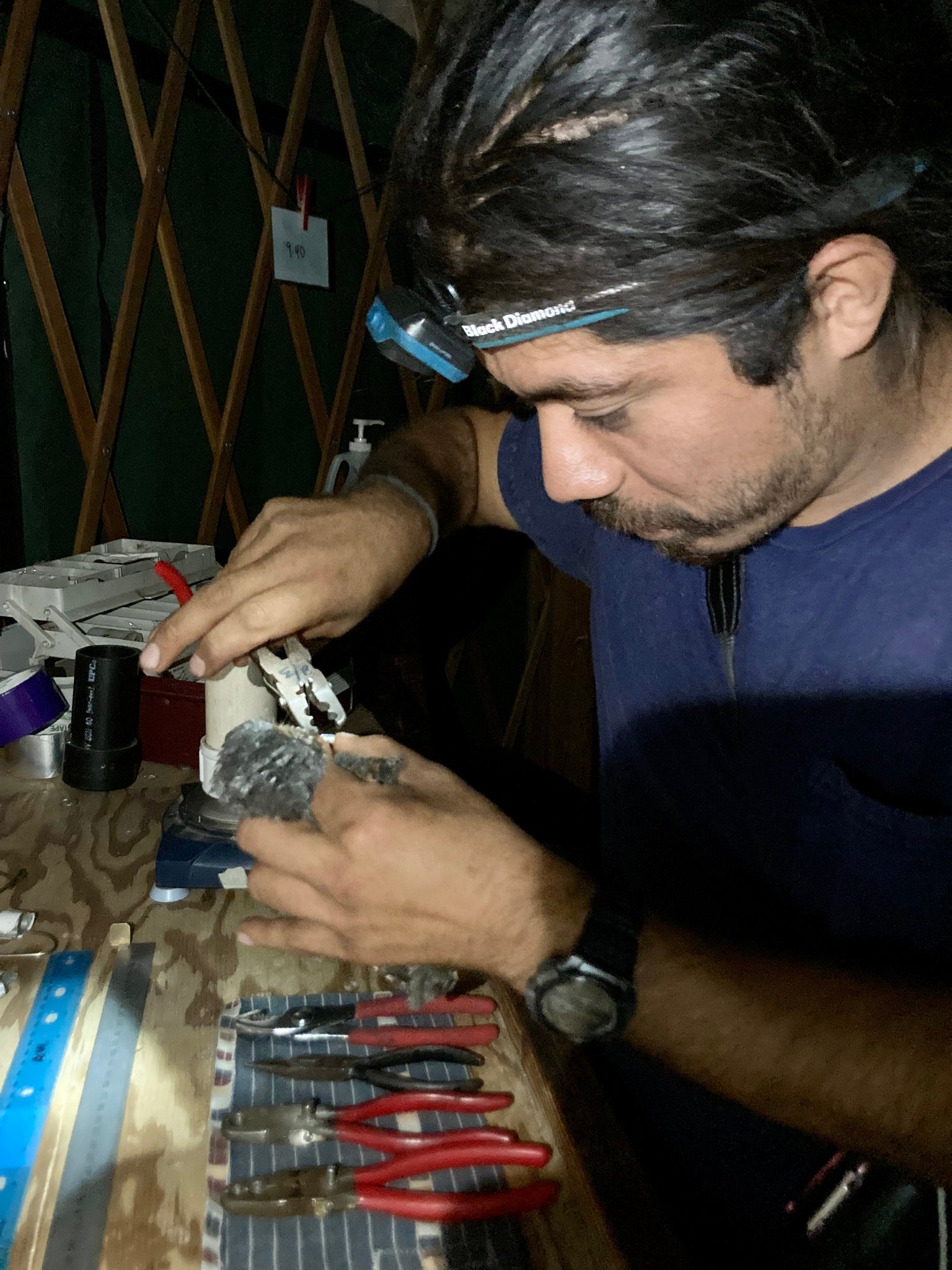 image shows a scientist wearing a headlamp holding a small brown bird in the left hand while using a pair of banding pliers in the right