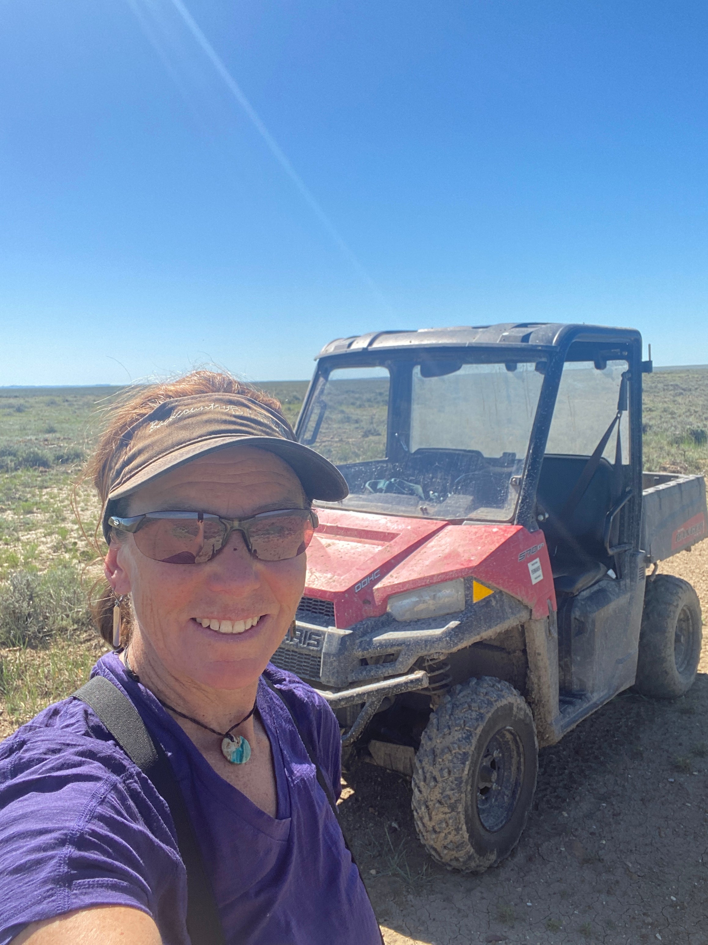 image show a biologist smiling for a selfie with a red UTV vehicle behind her