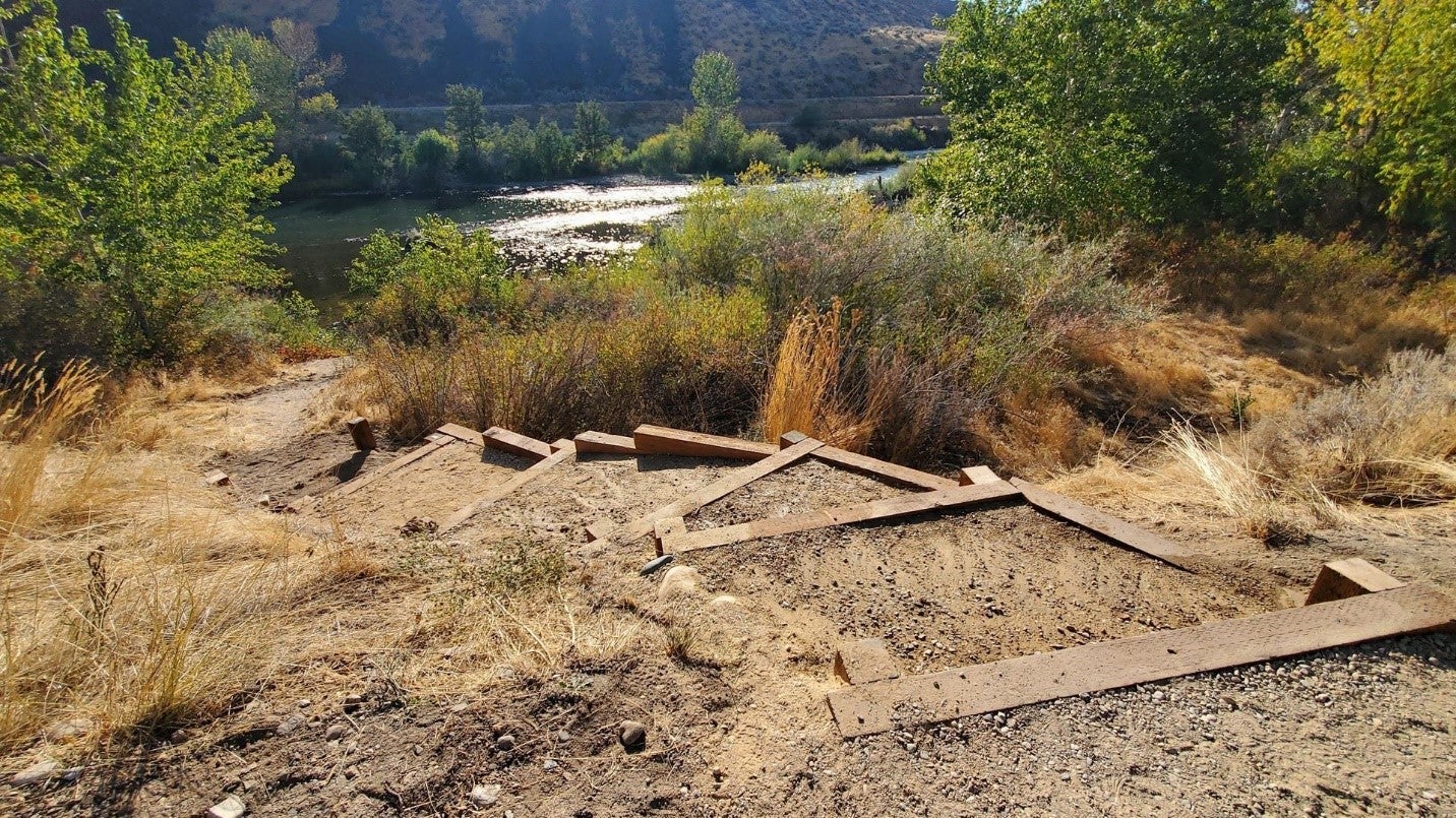 a view from the top of newly dug stairs made from lumber and hard packed dirt. The stairs stretch down the banks through willows, all the way to the Boise River