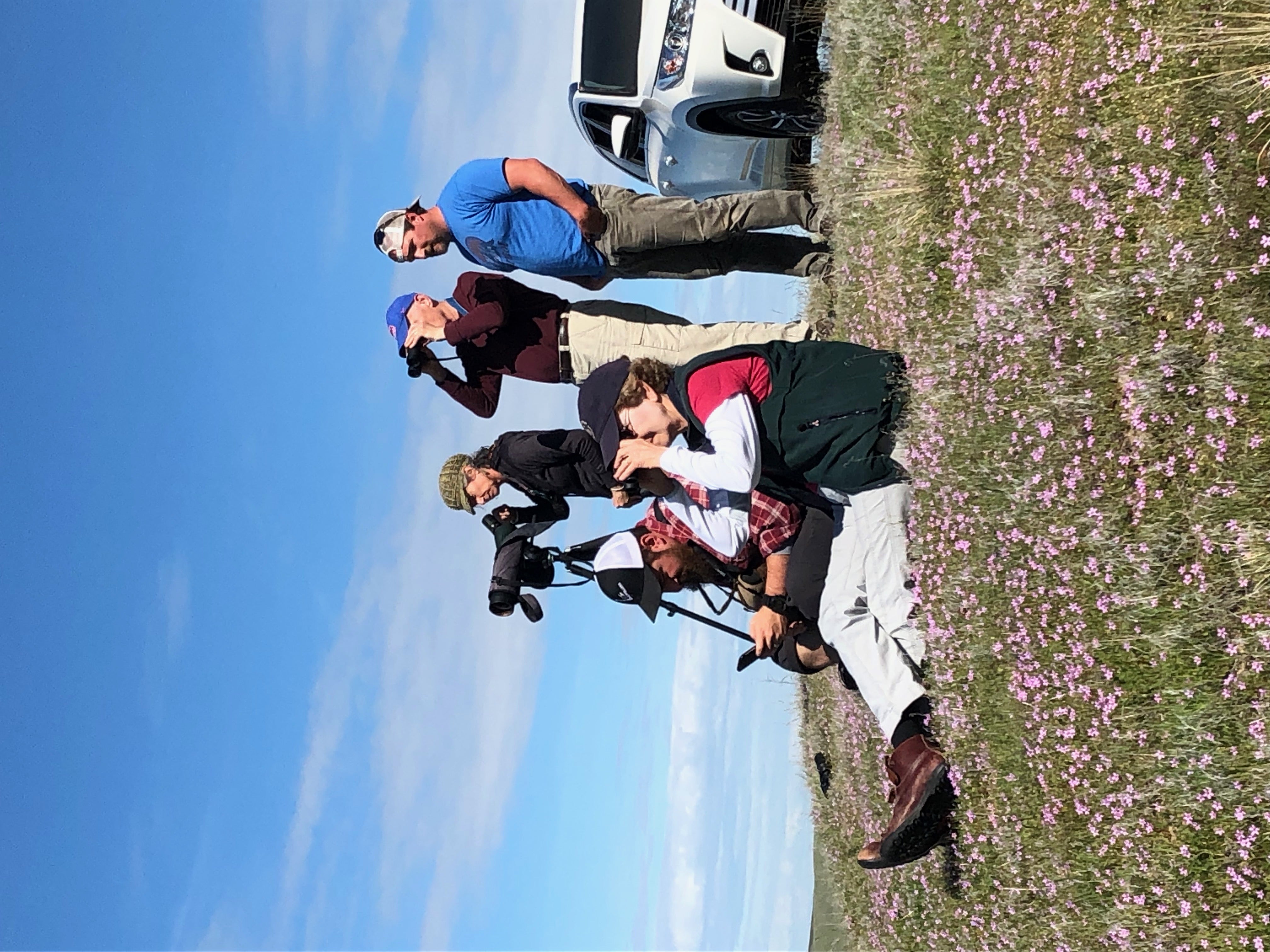a group of people stands outside looking through binoculars and spotting scopes
