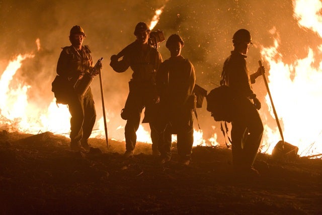 4 Firefighters holding equipment silhouetted against a fire burning in the background